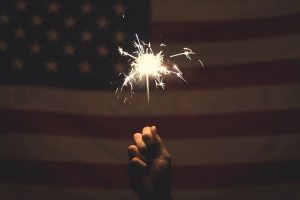 hand holding a sparkler in front of an American flag